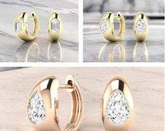 May include: A collection of gold hoop earrings with various gemstone settings. One pair features emerald-cut stones, another round-cut, and a third pair showcases pear-shaped gems. The earrings are displayed on a reflective surface.