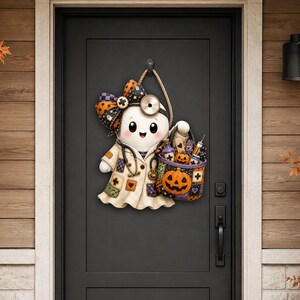 May include: A decorative door hanger featuring a cartoon ghost dressed as a doctor, wearing a white lab coat with colourful patches, a stethoscope, and a head mirror. The ghost holds a purple trick-or-treat basket filled with medical supplies and a pumpkin.