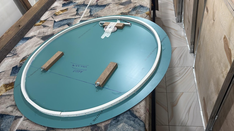Peut inclure: Un dos de miroir ovale pr&eacute;sentant une surface bleu sarcelle avec un bord de cadre blanc. Deux blocs de bois rectangulaires sont fix&eacute;s au centre, et un support de suspension en m&eacute;tal avec du ruban adh&eacute;sif blanc est plac&eacute; sur le bord sup&eacute;rieur.