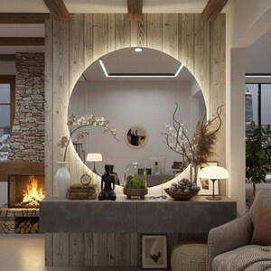 Peut inclure: Un grand miroir mural circulaire avec r&eacute;tro&eacute;clairage LED int&eacute;gr&eacute; mont&eacute; sur un mur en panneaux de bois verticaux. Le miroir refl&egrave;te l'int&eacute;rieur d'une pi&egrave;ce, tandis qu'une console grise en dessous porte un vase blanc, des livres et divers objets.