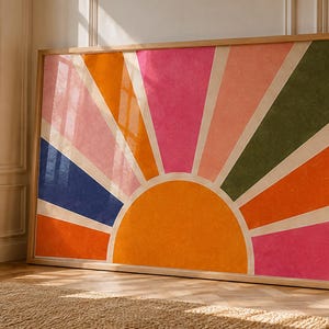 Peut inclure: Une grande impression d'art rectangulaire dans un cadre en bois clair présentant un motif de soleil stylisé. Le graphique se compose d'un demi-cercle orange central avec des rayons alternant les couleurs rose, orange, bleu foncé et vert olive.