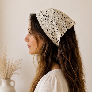 Può includere: Un foulard triangolare color crema caratterizzato da un intricato motivo all'uncinetto con dettagli ispirati ai fiori. L'accessorio è realizzato in filo sottile e presenta un delicato design traforato che copre la parte superiore.