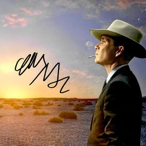 May include: A man in a suit and hat, smoking a cigarette, against a desert sunset backdrop. The image includes an autograph in black ink in the upper left corner. The sky transitions from orange to blue.