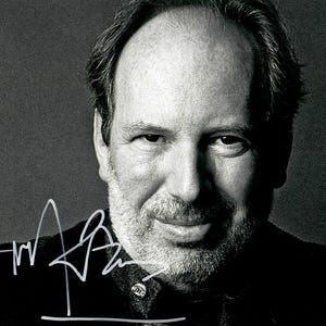 May include: Black and white portrait of a man with a signature. The man has short, dark hair and a beard. He is wearing a dark jacket. The signature is in white ink and is located on the lower left side of the image.
