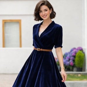 May include: A navy blue velvet dress with a wrap-style bodice, short sleeves, and a flared skirt. The dress is cinched at the waist with a brown belt. The dress is a midi length and is suitable for formal events.