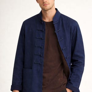 Peut inclure: Veste bleu marine avec col officier et fermetures à brandebourgs. La veste a des manches longues et deux poches avant. La personne porte un t-shirt marron sous la veste.