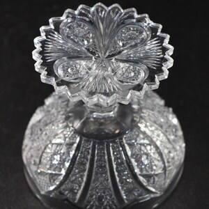 May include: A clear, cut-glass bowl with a detailed, textured pattern. The bowl features a scalloped rim and a decorative, starburst design on the base. The intricate cuts create a sparkling effect, reflecting light. The bowl is likely for serving or display.