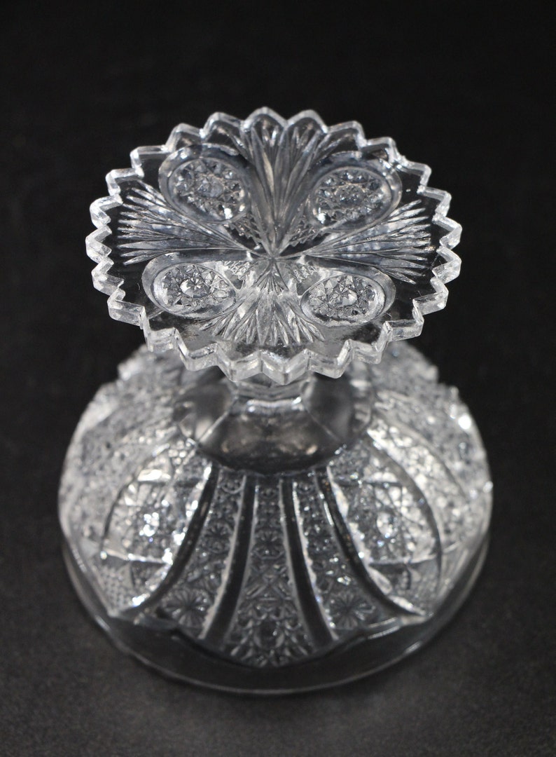 May include: A clear, cut-glass bowl with a detailed, textured pattern. The bowl features a scalloped rim and a decorative, starburst design on the base. The intricate cuts create a sparkling effect, reflecting light. The bowl is likely for serving or display.