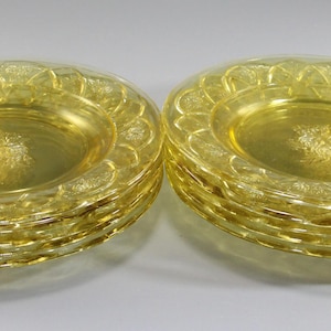 May include: Two stacks of yellow glass plates. Each plate has a scalloped edge and a floral design in the center. The plates are a light, transparent yellow color.