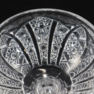 May include: Close-up of a clear, cut-glass bowl with intricate geometric patterns. The bowl features a detailed design of stars, diamonds, and fan-like shapes, creating a textured surface. The bowl's design is symmetrical and elegant.