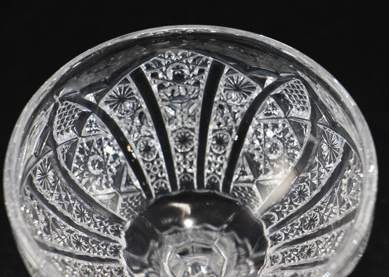 May include: Close-up of a clear, cut-glass bowl with intricate geometric patterns. The bowl features a detailed design of stars, diamonds, and fan-like shapes, creating a textured surface. The bowl's design is symmetrical and elegant.
