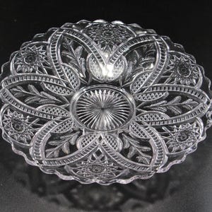 May include: Clear, oval-shaped glass serving dish with intricate, symmetrical patterns. The design includes starbursts, floral elements, and geometric shapes. The edges are scalloped, adding to the decorative appeal. A classic piece for serving appetizers or desserts.