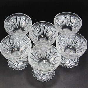 May include: Six clear glass dessert bowls with intricate cut crystal designs. Each bowl has a rounded shape, a pedestal base, and detailed patterns. The bowls are arranged on a black surface, showcasing their elegant craftsmanship.