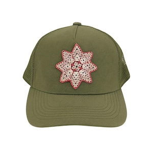 May include: Olive green trucker hat with a floral design. The hat features a mesh back and a curved brim. The floral design is a starburst shape with pink and white beads. The hat is a casual accessory.