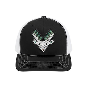 Puede incluir: Gorra de camionero en blanco y negro con un diseño cosido de una cabeza de cabra estilizada. El panel frontal es negro con una cabeza de cabra blanca y verde. La parte trasera de malla es blanca y la visera es negra con costuras blancas.