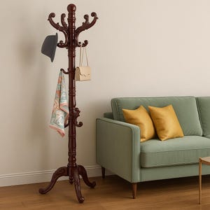 May include: A dark brown wooden coat rack with multiple hooks and decorative carvings. A gray hat, a beige purse, and a patterned scarf hang from the hooks. The coat rack is in a room with a green sofa and yellow pillows.