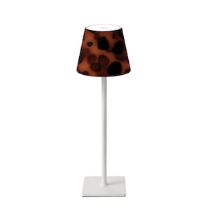 May include: A modern table lamp with a white base and stem, topped with a lampshade featuring a brown and black spotted pattern. The lamp has a square base and a cylindrical lampshade, suitable for home decor.