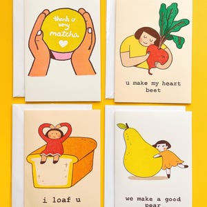 May include: Four illustrated greeting cards with text on a yellow background. The cards feature a matcha, beet, loaf of bread, and pear with the phrases "thank u very matcha", "u make my heart beet", "i loaf u", and "we make a good pear".