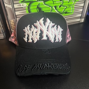 May include: Black trucker hat with a white and pink embroidered design. The hat features the text "KOYK" in white and pink, with "HOPE AWAKENINGS" embroidered on the brim. The mesh backing is pink with a star pattern.