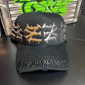 May include: Black baseball cap with silver and gold-colored metal embellishments. The cap features the text "HOPE AWAKENS" embroidered on the brim. The background includes graffiti art.