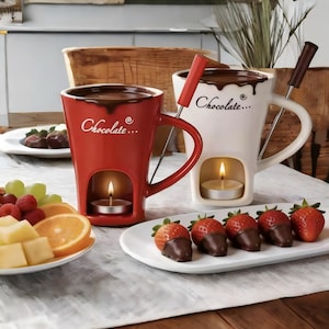 Könnte beinhalten: Ein roter und ein weißer Keramik-Schokoladenfondue-Becher, jeweils mit dem Schriftzug "Chocolate..." und einer Aussparung für ein Teelicht. Die Becher enthalten eine Metallgabel und werden von Tellern mit frischen Erdbeeren und Orangenscheiben begleitet.