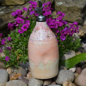 May include: A ceramic oil cruet with a glossy finish featuring a gradient of soft peach and cream tones. The bottle has a rounded body and is topped with a silver-coloured metal pourer spout with a black rubber seal and a small hinged lid.