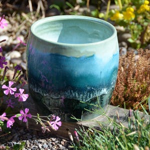 May include: A cylindrical ceramic vessel featuring a smooth, glossy glaze that transitions from a pale mint green at the rim to a deep, saturated teal and dark forest green at the base, with a subtle drip effect visible along the lower section.