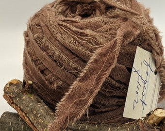 May include: A brown frayed ribbon spool with a tag that says "Reetha  Morocco". The spool is sitting on two brown sticks.