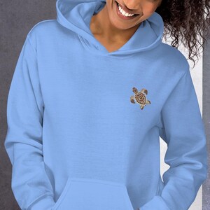 Può includere: Felpa con cappuccio azzurra con tasca frontale e cappuccio con coulisse. La felpa presenta un piccolo disegno ricamato di tartaruga marina sulla parte superiore sinistra del petto. La tartaruga marina è marrone e beige.