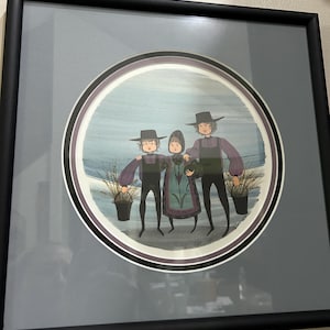 May include: A framed circular print featuring three figures in dark hats and period clothing standing in a field. The two outer figures hold black buckets, while the central figure wears a patterned apron. The artwork is set against a blue background.