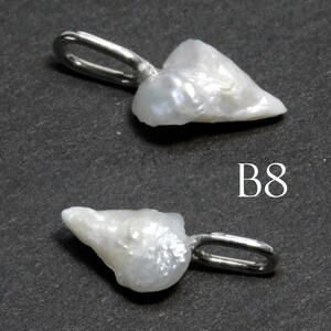 May include: Two white, irregularly shaped pearl pendants with silver-colored loops for hanging. The pendants are set against a dark gray background. The text "B8" is visible in white.