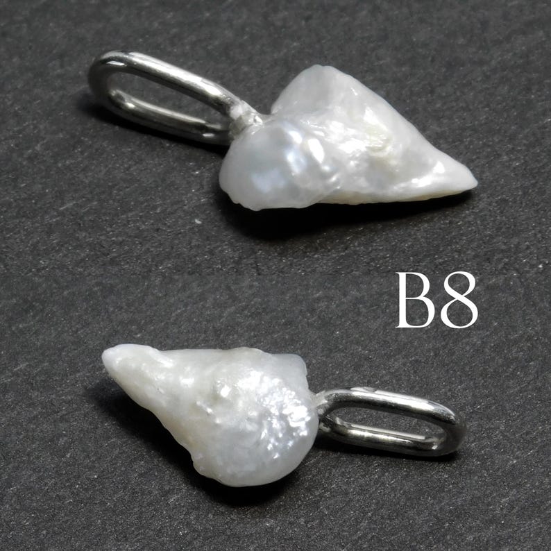 May include: Two white, irregularly shaped pearl pendants with silver-colored loops for hanging. The pendants are set against a dark gray background. The text "B8" is visible in white.