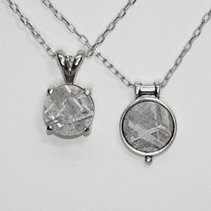 May include: Two silver necklaces with meteorite pendants. One pendant is a round stone held by four prongs. The other pendant is a round stone set in a silver bezel with a small decorative bead at the bottom.