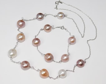 May include: A silver chain necklace with a variety of pink, white, and peach pearls. The necklace is layered and has a clasp.