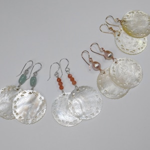 May include: Three pairs of earrings with carved shell pendants. The top pair features a pink pearl and a rose gold hook. The middle pair has orange beads and silver hooks. The bottom pair has green beads and silver hooks.
