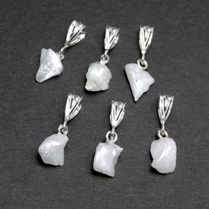 May include: Six white gemstone pendants with silver bail settings. The gemstones are irregular in shape and have a milky white color.
