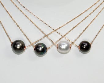 May include: Four necklaces with different colored pearls. Each necklace has a gold chain and a single pearl pendant. The pearls are black, green, white, and black.
