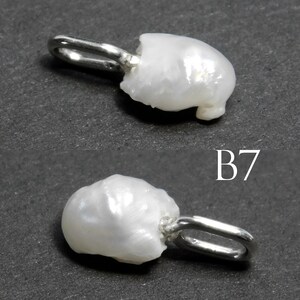 May include: Two white baroque pearl pendants with silver-tone bails. The pearls have an irregular shape and a lustrous surface. The pendants are displayed against a dark gray background. The text "B7" is visible.