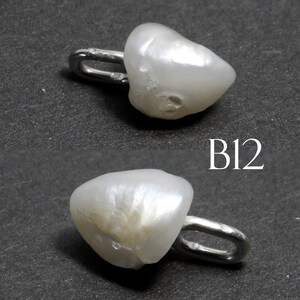 May include: Two white, irregularly shaped pearl pendants with a silver-colored loop attached. The pendants are on a dark gray surface. The text "B12" is in white on the surface.