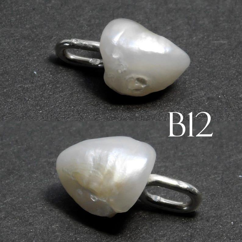May include: Two white, irregularly shaped pearl pendants with a silver-colored loop attached. The pendants are on a dark gray surface. The text "B12" is in white on the surface.