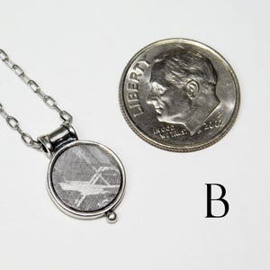 May include: A silver-toned necklace with a round pendant featuring a patterned, gray stone. A U.S. dime is next to the pendant for size comparison. The pendant is approximately 0.75 inches in diameter.