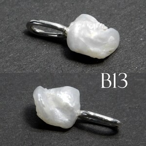 May include: A white, irregularly shaped pearl pendant with a silver-colored loop. The pendant has a natural, organic form and a lustrous surface. The image also includes the text "B13".