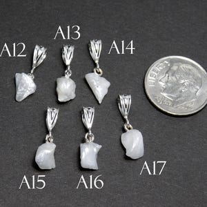 May include: Seven silver pendants with white, opaque, irregular shaped stones. The pendants are labeled A12, A13, A14, A15, A16, and A17.