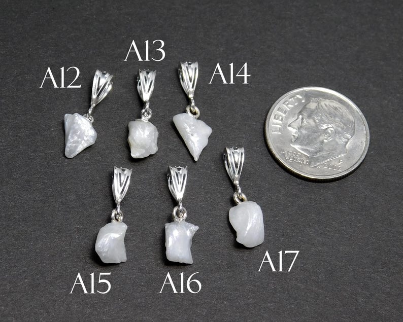 May include: Seven silver pendants with white, opaque, irregular shaped stones. The pendants are labeled A12, A13, A14, A15, A16, and A17.