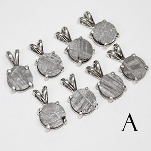 May include: A collection of nine silver-toned pendants with a round, textured, gray stone center. Each pendant has a loop at the top for a chain. The letter "A" is in black at the bottom right.