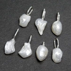 May include: Seven irregularly shaped, white freshwater pearl pendants with silver-colored bails are displayed against a dark gray background. The pearls have a lustrous, organic texture, and each bail is a simple, curved design.