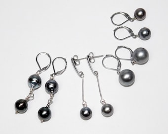 May include: An assortment of pearl earrings in various styles. The earrings feature dark gray and black pearls, with silver-toned metal hooks and chains. Some earrings have multiple pearls, while others have a single pearl.