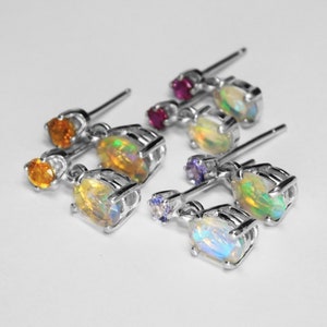 May include: A set of six silver earrings with opal and gemstone accents. Each earring features a small, oval-shaped opal stone with a colorful iridescent sheen. The opal stones are accented with small, round gemstones in various colors, including purple, pink, and yellow.