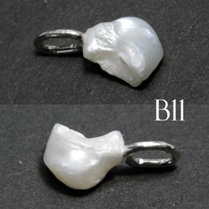 May include: A white, irregularly shaped pearl pendant with a silver-colored bail. The pendant has a natural, organic form and is shown against a dark background. The text "B11" is visible.