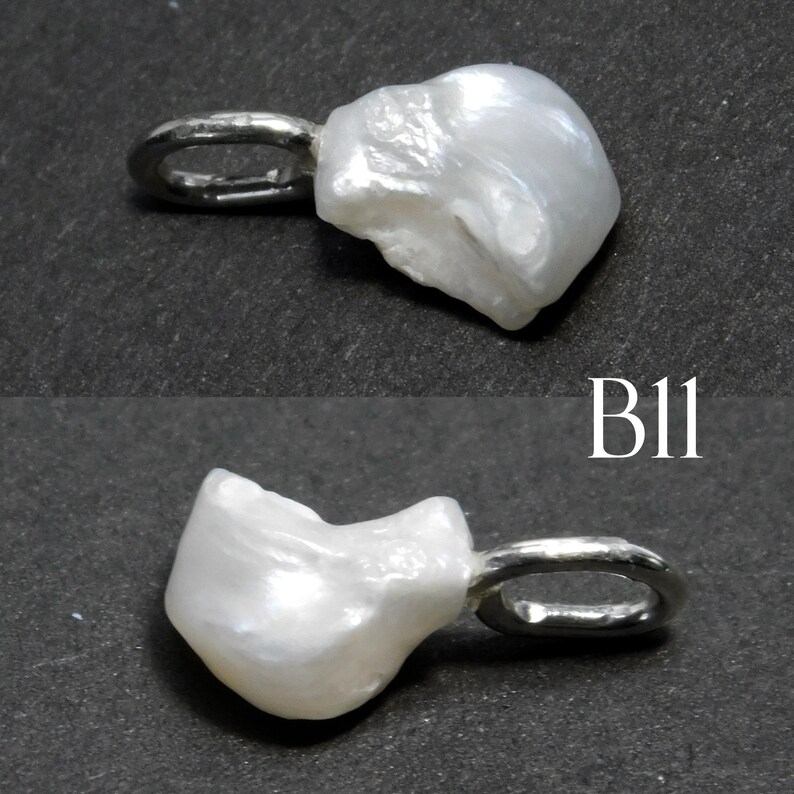 May include: A white, irregularly shaped pearl pendant with a silver-colored bail. The pendant has a natural, organic form and is shown against a dark background. The text "B11" is visible.